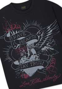 Black shirt with a detailed print of an eagle clutching a heart, banners reading "Brave Hearts" and "Stay True," and text "Love Kills Slowly."