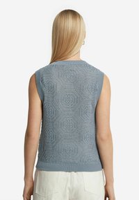 Ljusblå ärmlös stickad tröja med ett intrikat hexagonalt mönster, ribbad halsringning och nederkant samt en texturerad yta.