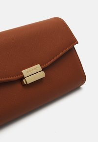 Porte-monnaie en synthétique texturé marron avec un fermoir doré et le logo "ANNA FIELD" en avant. Forme rectangulaire, finition lisse.