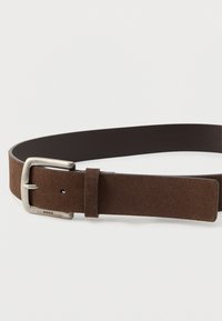 Cinto de camurça castanho com um acabamento texturizado, apresentando uma fivela de metal prateado e um laço de couro. Etiqueta da marca "HUGO" gravada no couro.