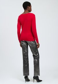 Maglione rosso attillato a maniche lunghe abbinato a pantaloni svasati argentati lucidi. Il maglione ha un collo rotondo; i pantaloni presentano cuciture laterali.