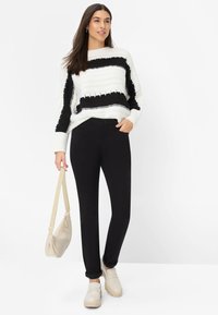 Chunky gebreide trui in wit met zwarte strepen, gecombineerd met nauwsluitende zwarte broek. Beige crossbody tas en lichtgekleurde schoenen maken de outfit compleet.