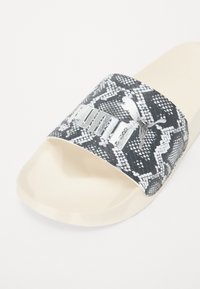 Svarte og hvite slangeskinnmønstrede sandaler med myk, kremfarget såle og en fremtredende sølvfarget Puma-logo på stroppen.