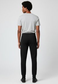 Pantalones deportivos negros con cintura y puños elásticos, combinados con una camiseta ligera gris. Textura suave, diseño casual.