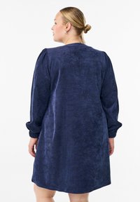 Námořnické modré šaty z měkké, texturované látky s uvolněným střihem, nadýchanými rukávy a nabíranými manžetami. Jednoduchý design, silueta do kolen.