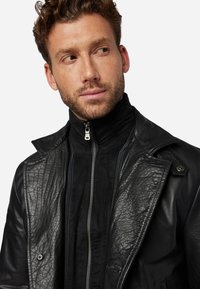 Black leather jacket featuring a textured finish, large lapels, and a zippered front. The inner layer has a smooth, black fabric.