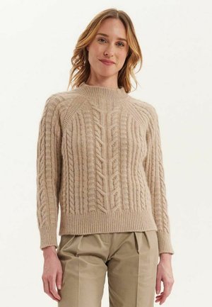 Pull en maille beige avec un col montant, présentant des motifs en câble et des poignets côtelés. Composé de fil doux, il a une finition texturée.