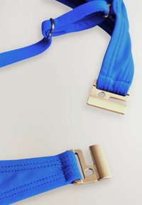 Blaue verstellbare Träger aus strukturiertem Stoff, ausgestattet mit goldfarbenen Metallverschlüssen und Nähdetails für eine sichere Befestigung.