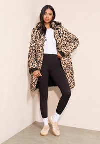 Ilvesemustriga puffermantel kapuutsiga, mustade detailide ja lõdva lõikega, kombineeritud mustade retuuside ning beežide spordijalatsitega valgete sokkidega.