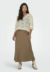 Pull en maille crème avec une coupe ample et une texture à motifs, associé à une longue jupe en satin marron et des bottines beiges.