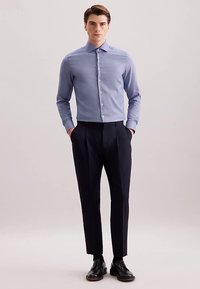 Lichtblauw overhemd met knopen en een puntige kraag, gecombineerd met donkerblauwe broek. Het overhemd heeft een textuurpatroon en lange mouwen.