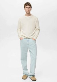 Pulover crema, blugi deschiși la culoare și papuci bej. Design simplu cu mâneci ajustate și croială dreaptă.