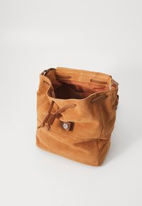 Sac bourse en daim couleur fauve avec une fermeture à cordon et des accents en cuir. Intérieur spacieux avec une poche unique et des détails en métal.