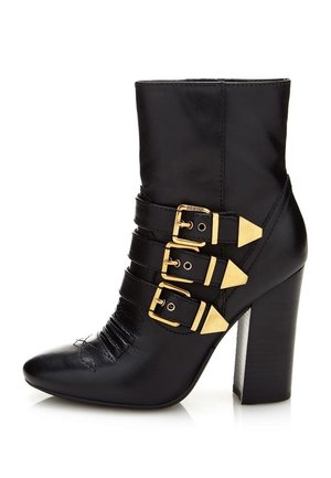 Schwarzer Leder-Stiefelette mit drei goldenen Schnallen, spitzer Zehe und klobigem hohen Absatz.