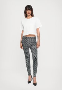 White cropped t-shirt, black leggings with repeating gray logo pattern, and black high heels. Smooth texture, fitted design.