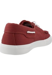 Zapatilla de lona roja con suela de goma blanca, diseño con cordones y costuras en contraste. La vista trasera revela una textura suave y un branding mínimo.
