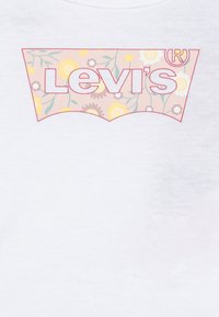 T-shirt bianca con un logo Levi's rosa e floreale in una forma di etichetta sovradimensionata a contrasto. Il design include fiori e foglie multicolori.