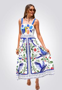 Abito maxi bianco con motivi floreali e di uccelli in blu, verde e rosso, caratterizzato da un corpino aderente, spalline larghe e rifiniture decorative.