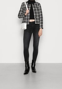 Mustat ja valkoiset ruudulliset takki, lyhyt musta neule, mustat kiiltävät farkut ja mustat korkokengät. Kantaa pientä valkoista olkalaukkua.