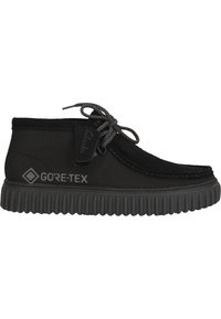 Black GORE-TEX footwear with a suede upper, featuring a rubber sole, minimal lacing, and textured detailing on a rounded edge.