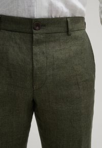 Groene linnen broek met een gestructureerde afwerking, voorzien van een knoopsluiting en rechte pijpen. De tailleband heeft riemlussen voor extra functionaliteit.