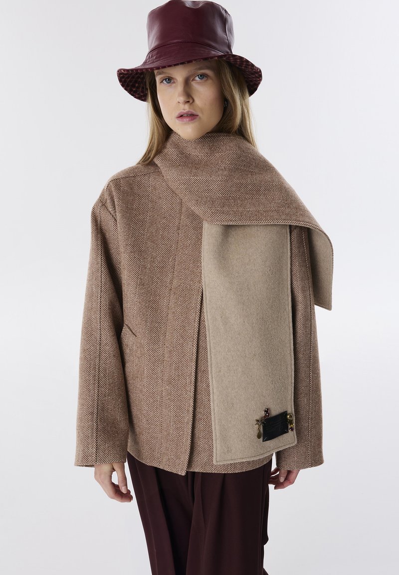 Bruine visgraatjas met een beige accent-sjaal, leren bordeauxrode hoed, losse pasvorm, gestructureerde stof, voorzien van decoratieve hardware aan de zijkant.