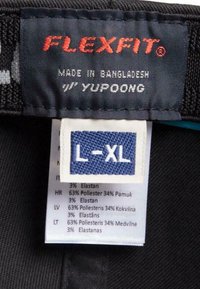 Crna tkanina oznaka s crvenim logom "FLEXFIT", koja sadrži više oznaka za njegu koje detaljno opisuju sastav materijala, veličinu L-XL i zemlju podrijetla.