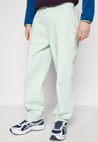 Light mint green trousers made of cotton with a relaxed fit, featuring side pockets and belt loops, paired with navy and white sneakers.