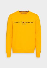 Sudadera amarilla de algodón, con "TOMMY HILFIGER EST. 1985" en texto negro, cuello redondo y puños acanalados con detalle del logo.