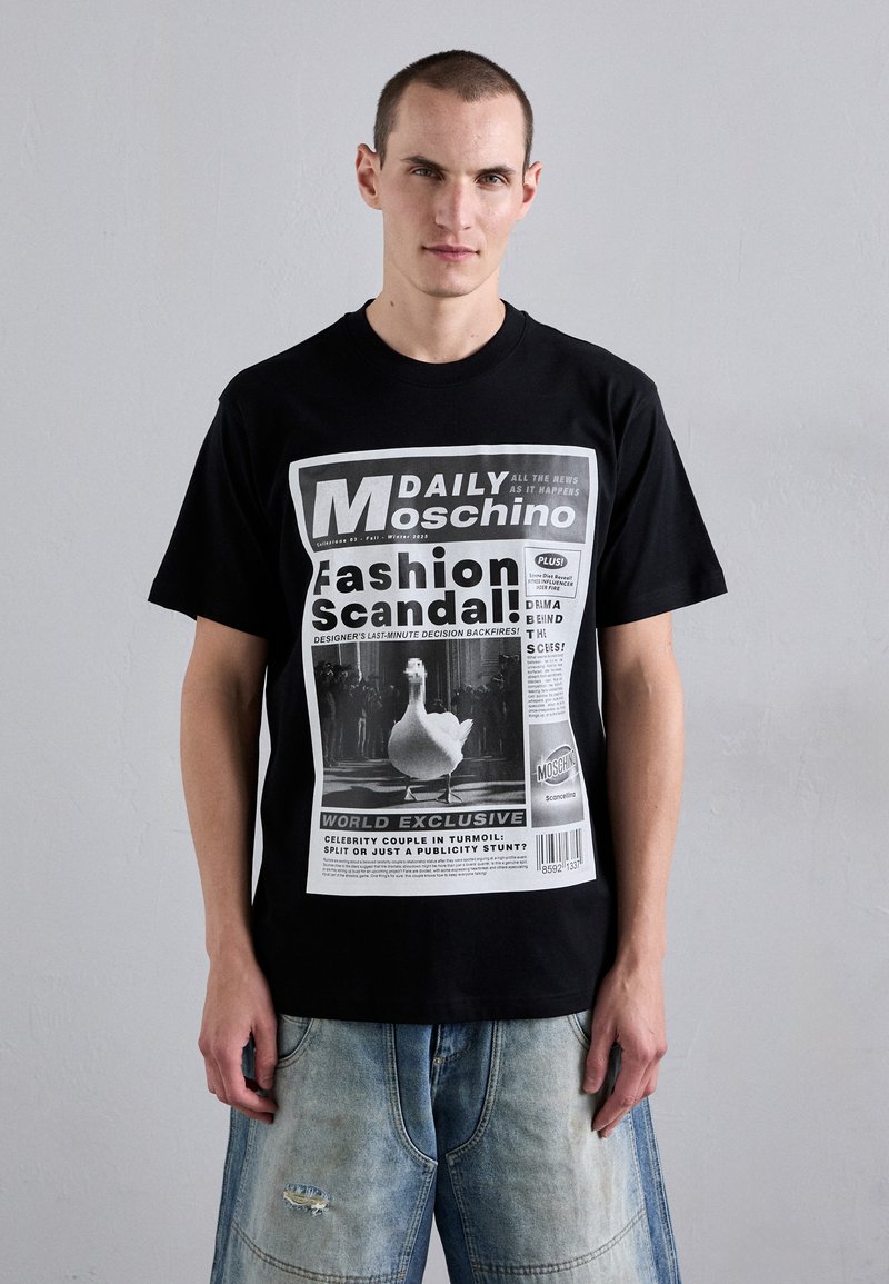 Tricou din bumbac negru, cu un design imprimat de ziar în alb, centrat în jurul unei imagini cu o rață, având text și elemente grafice îndrăznețe.