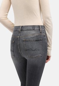 Szare dżinsy z denimu o dopasowanym kroju, z dwoma tylnymi kieszeniami, widocznymi przeszyciami oraz metką marki na pasie.