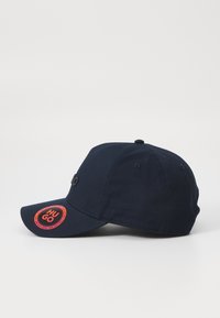 Marineblaue Kappe mit einem gekrümmten Schirm, die auf der Seite ein rotes, rundes Logo mit der Aufschrift "HU GO" und ein kleines schwarzes Akzentlogo auf der Vorderseite hat.