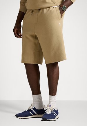 Beige bomullsshorts med elastisk midje og snøring. Kombinert med marineblå sportsko, hvite sokker og en uformell collegegenser.