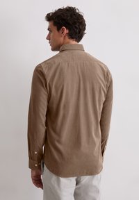 Brązowa koszula z długim rękawem, z klasycznym kołnierzykiem i gładką fakturą. Koszula ma zaokrąglony dół i guziki jako akcenty.