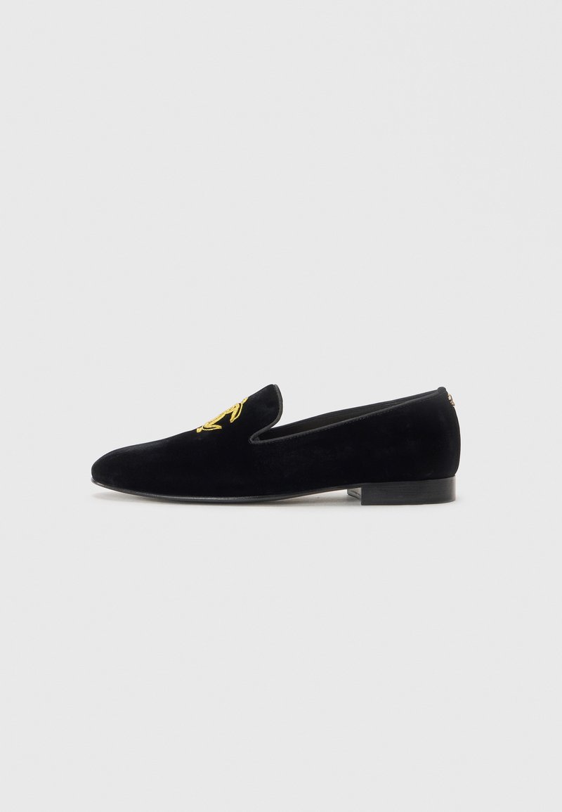 Svart sammet herr loafers med guld broderade initialer på toppen och en låg staplad klack, visad i sidoprofil mot vit bakgrund.