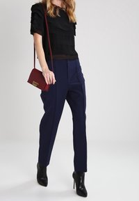 Černý vrstvený top s krátkým rukávem, námořnické elegantní kalhoty a černé kotníkové boty na podpatku. Červená křížová taška se zlatými kovovými detaily.