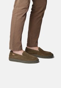 Hnědé semišové slip-on boty s pletenou juteovou podrážkou, s kulatou špičkou a ozdobným prošitím podél horního okraje.