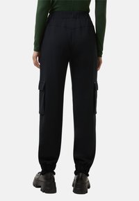 Achteraanzicht van een persoon in zwarte cargojoggingbroeken met elastische boorden en zwarte chunky schoenen, gecombineerd met een groen shirt met lange mouwen.