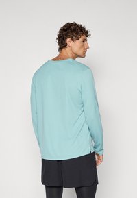 Lysblå langærmet skjorte med rund halsudskæring og sidesplitter, parret med sorte shorts. Blødt, glat stof med en afslappet pasform.