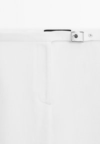 Witte broek met een rechte pasvorm, gestructureerde stof, een zichtbare riemlus en een zilveren metalen gesp. Bevat een voorkeurszak.