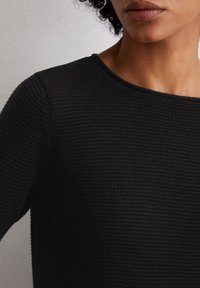 Schwarzer strukturierter Strickpullover mit Rundhalsausschnitt und geripptem Saum, der subtile Variationen in der Webdichte aufweist. Nahaufnahme.