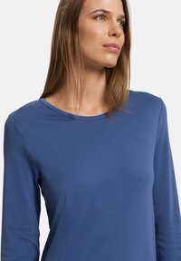 Camisa de manga larga azul hecha de una tela suave, con un escote redondo y un diseño ajustado. Textura lisa, sin patrones ni acentos visibles.