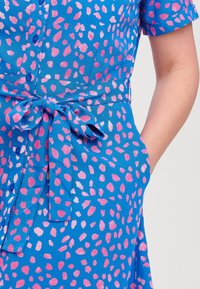 Abito blu con un motivo a pois in rosa e bianco, maniche corte, chiusura con bottoni e cintura in vita con tasche.
