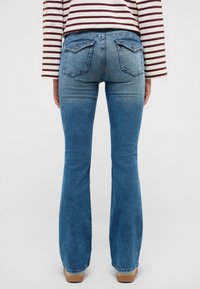 Flared blue denim jeans with a faded finish, featuring two back pockets and a straight leg design, paired with a striped top.