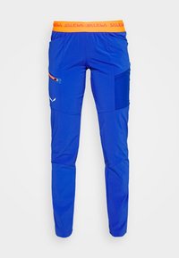 Siniset ulkoiluhousut oranssilla joustavyöhykkeellä, vetoketjullinen sivutasku ja erottuvat kangaspaneelit. Kevyt materiaali, jolla on sileä rakenne.