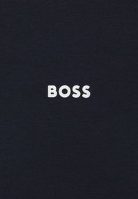 Jūras zilas kokvilnas krekls ar izteiksmīgu baltu "BOSS" logotipu centrā, ar gludu, vienveidīgu tekstūru un apaļu izgriezumu.