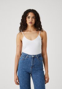 Hvit cami med justerbare spaghetti-stropper, kombinert med høyt liv blå denimjeans med dekorativ hvit nagling.