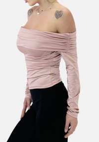 Axelbandslös, långärmad topp i mjukt rosa tyg med rynkad detaljering. Matchas med svart högmidjade leggings.