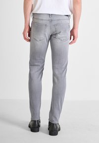 Jeans de mezclilla gris con un ajuste slim, que presentan un diseño clásico de cinco bolsillos, ligero desvanecimiento y costuras contrastantes. Zapatos de cuero negros visibles.