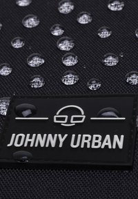 Tissu noir avec des gouttes d'eau ; présente un patch logo en relief portant "JOHHNY URBAN" en blanc contre le fond texturé.